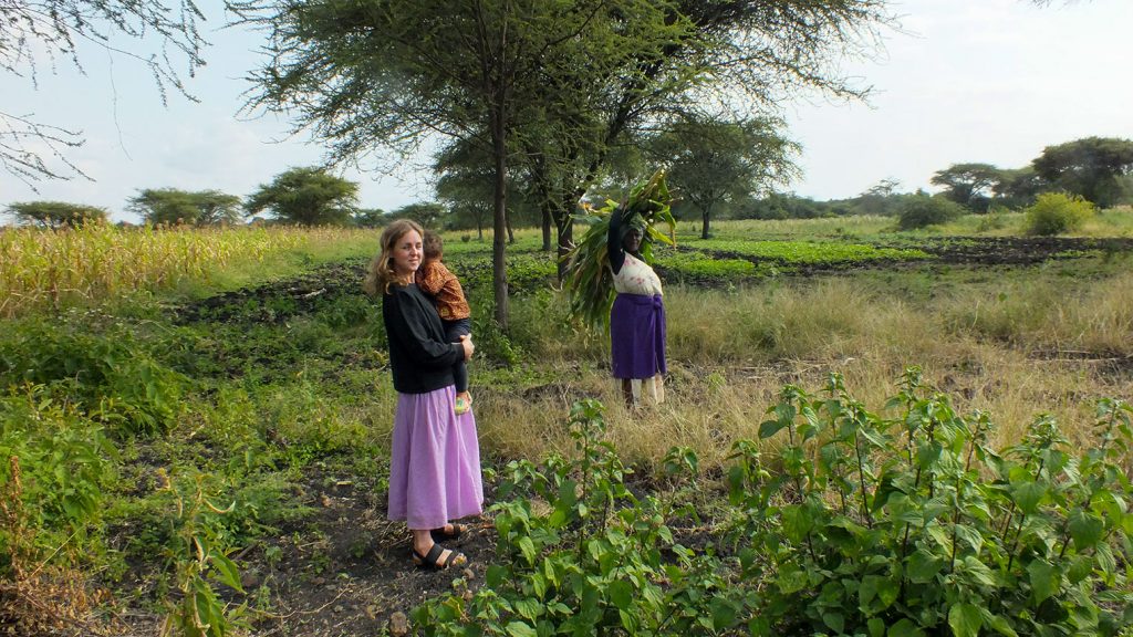 Tanzanian farmers and digital tech: two women, one holding a child and the other a bundle of sticks, in a field in Tanzania.